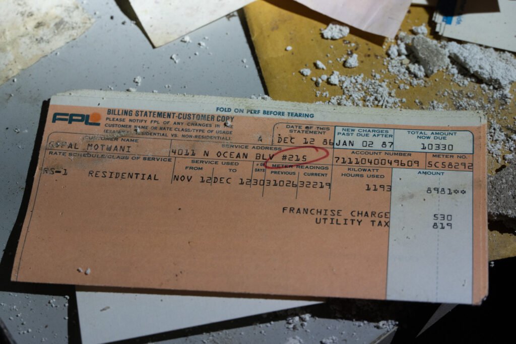 Old FPL billing statement from December 12, 1986, discovered at the abandoned Port of the Islands Hotel in Naples, FL, which has since been demolished. The bill, addressed to Gopal Motwani, shows residential service details with a total amount due of 3.30. Partially covered in debris, it highlights the decay and abandonment of the once-standing hotel.